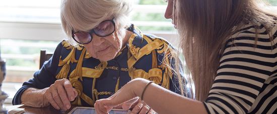 Two women sat together, one assisting the other with navigating an iPad.