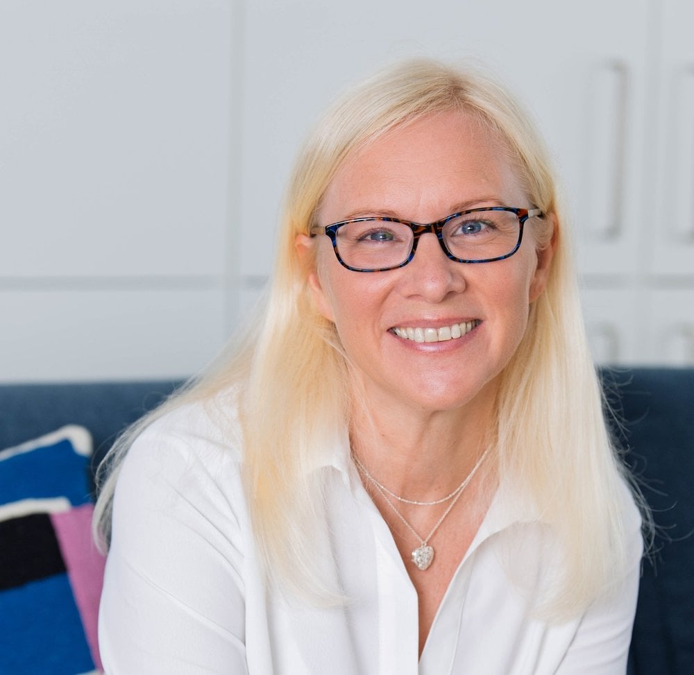 Hattie, sitting on a couch looking at the camera smiling.
