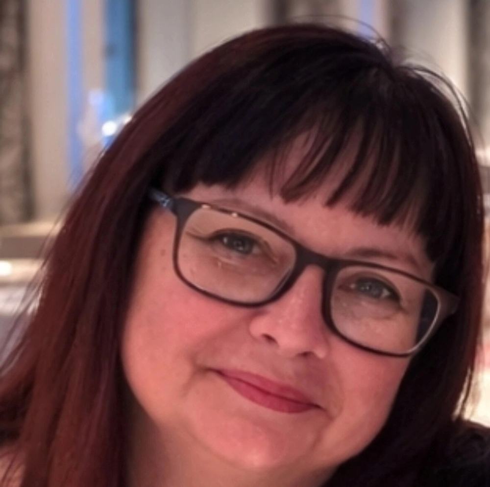 Sharon Ellis. A white woman with dark hair cut into a bob with a fringe. She is smiling softly at the camera. She's wearing glasses with black frames.