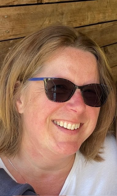 Female, blond shoulder length hair, wearing glasses and smiling