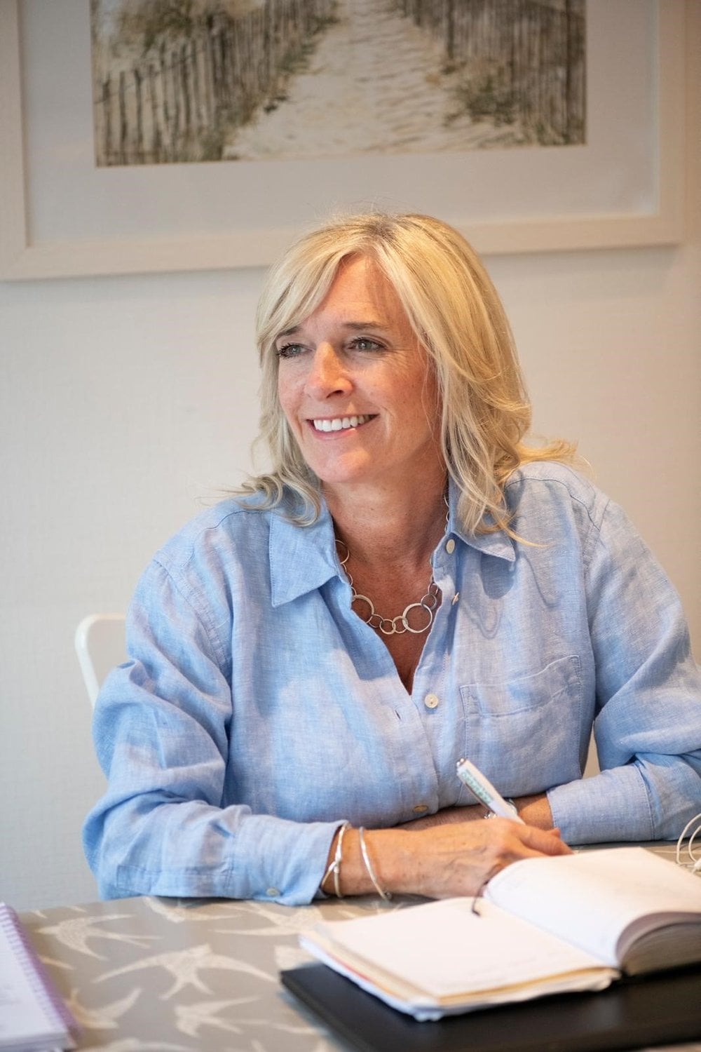 Photo of myself with blonde hair, sat at a desk, wearing a light blue shirt, smiling.