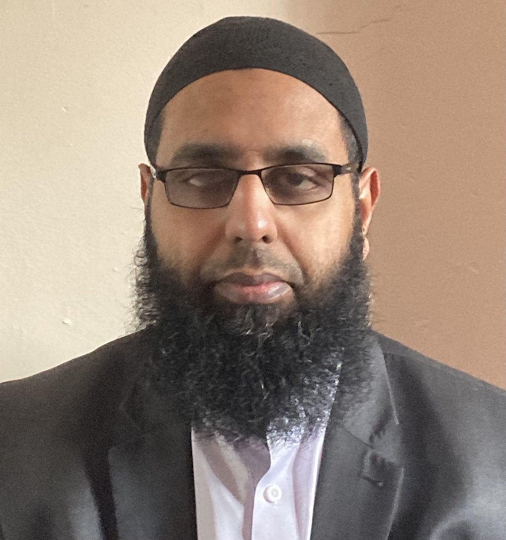 Front-facing image of Usmaan Rafiq, wearing a grey suit, light-coloured shirt, and glasses.