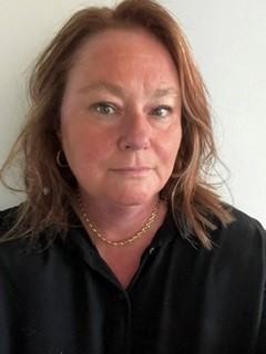 An image of Amanda Hawkins facing the camera, with shoulder-length hair, a black shirt, and gold necklace.