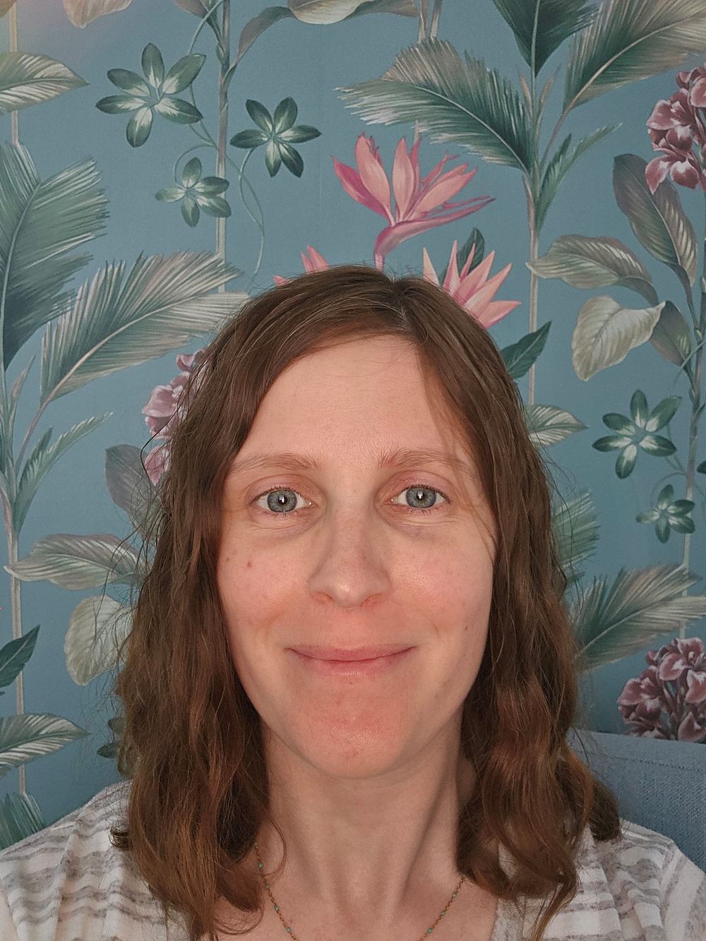 Counsellor Laurel Deegan in front of blue wallpaper with tropical plants and leaves on it.
