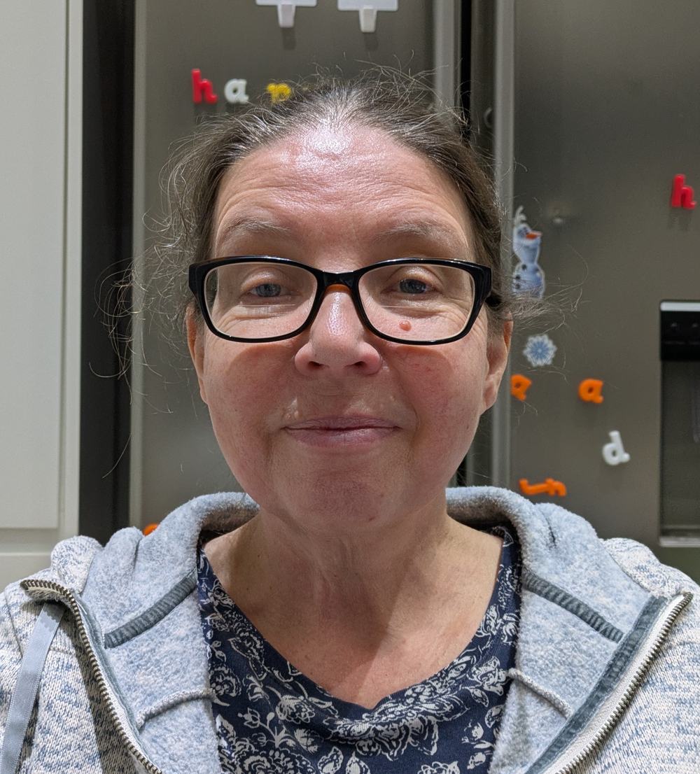 A woman with back framed glasses looking towards the camera while smiling.