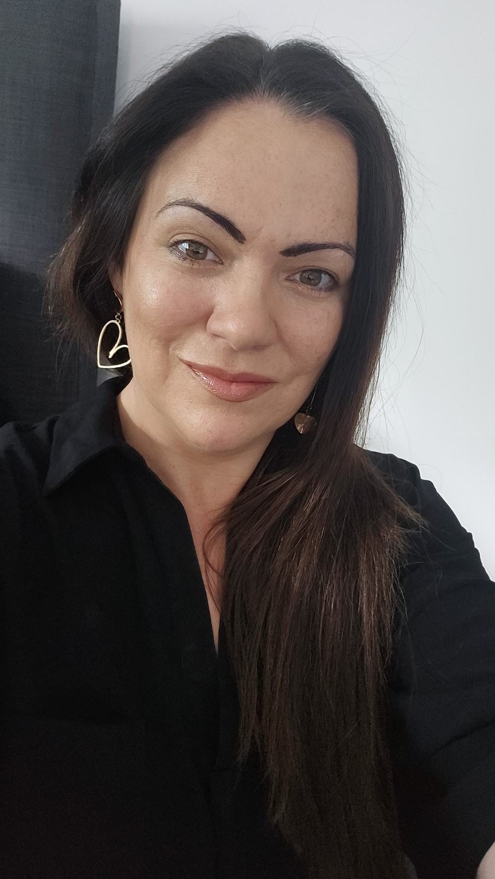 A woman, Karolynne Senior, is facing the camera and smiling. She has long dark hair and is wearing a black shirt with silver earrings.
