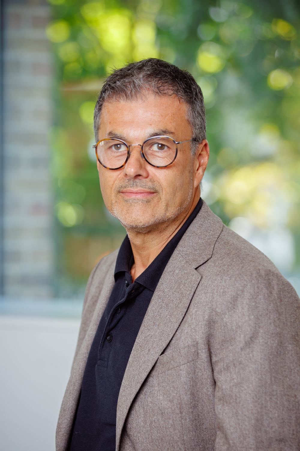A picture of Barry Hoffman, a man with short black and grey hair wearing glasses, a dark shirt and light stone suit jacket, smiling at the camera.