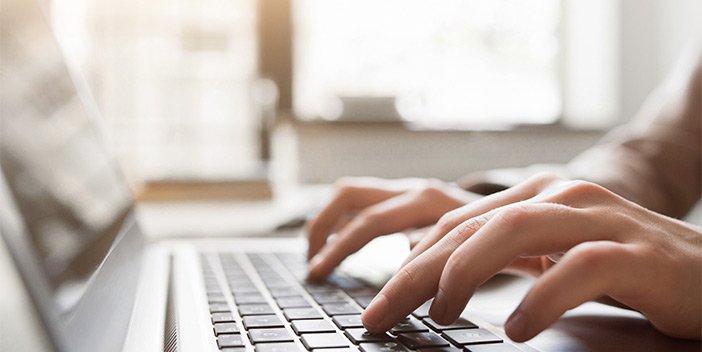 A closeup of hands as they type on a laptop keyboard, showing how you can stay at home by volunteering remotely for RNIB.