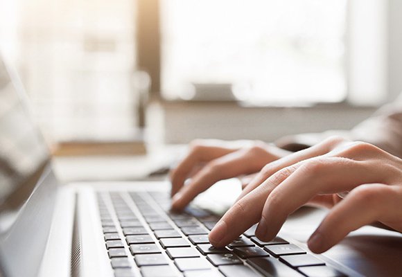 A closeup of hands as they type on a laptop keyboard, showing how you can stay at home by volunteering remotely for RNIB.