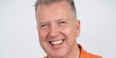Close up of Allan infront of a white background, wearing an orange top.