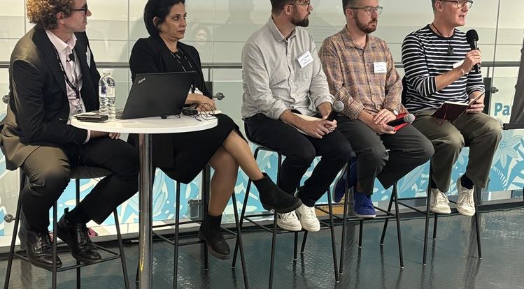 The Audio is King panel sitting on tall chairs next to one another in a line, in front of a large glass window in an office. From left to right they are John Paton and Sonali Rai from RNIB, Richard Kurzik from BBC, Jonathan Penny from Channel 4 and Simon Elder from Sky.