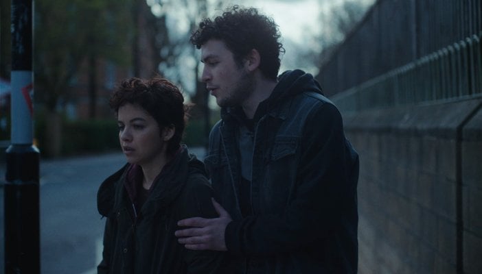 Girl and boy on the side of a street by a lamp post with a grey sky setting