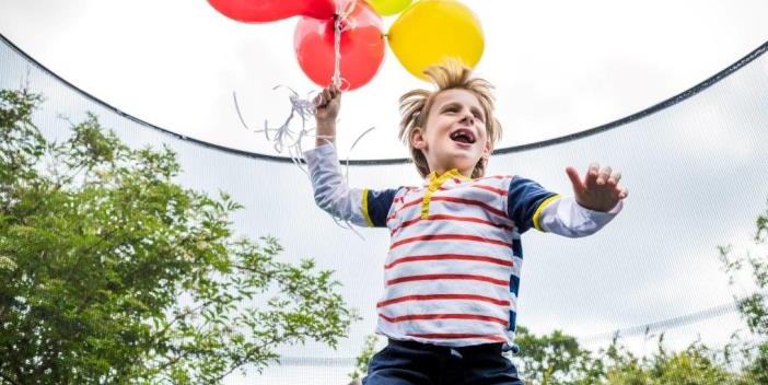 A child running while holding a bunch of balloons.
