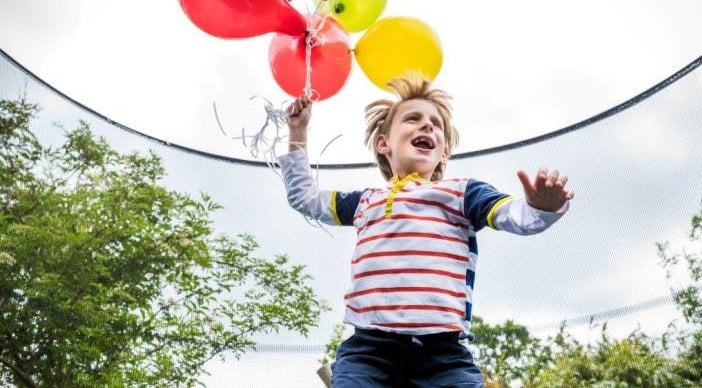 A child running while holding a bunch of balloons.