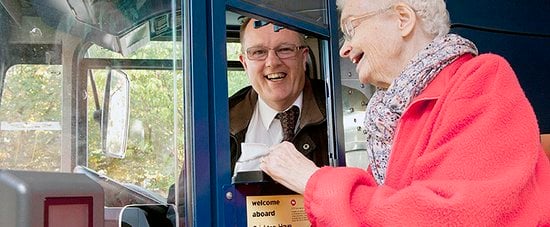 An older woman talking to a bus driver while showing him a note.