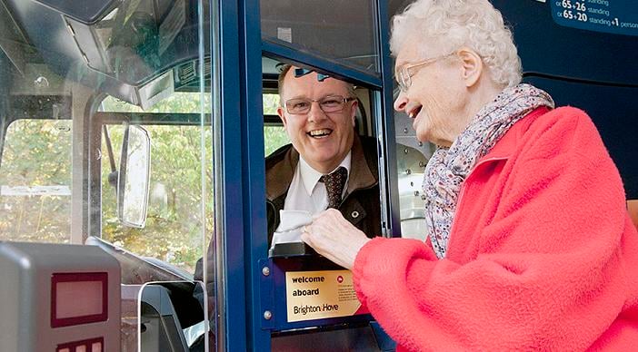 An older woman talking to a bus driver while showing him a note.
