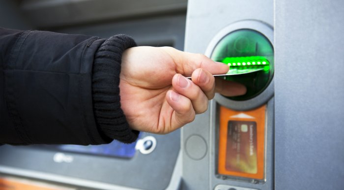 A close up of a person’s hand inserting a card into an ATM.