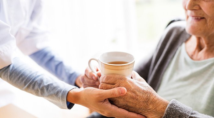 A carer handing a cup of tea to an older person.