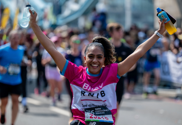 A person smiling with their arms in the air holding water bottles, taking part in a Challenge Event wearing an RNIB t-shirt.