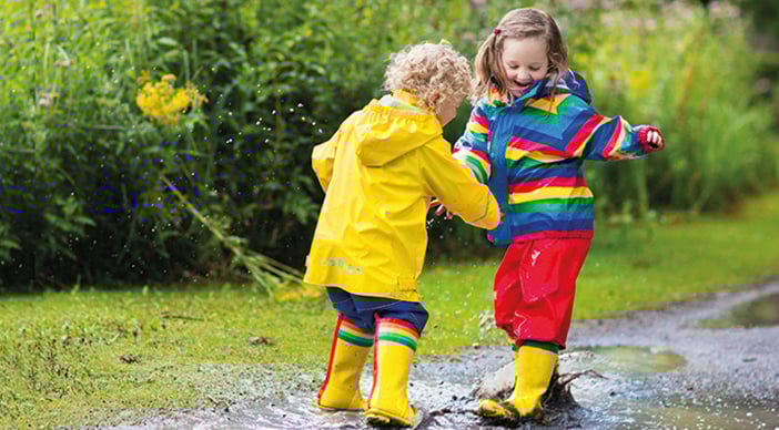 Two children in waterproofs and wellies play in a muddy puddle