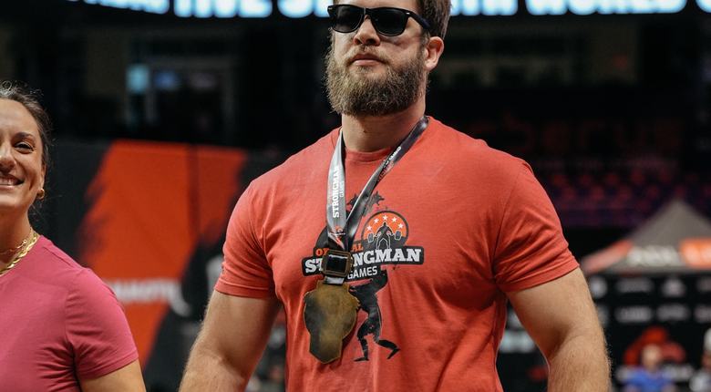 Evan, wearing dark glasses, walks with his wife Liz. He is wearing a medal from the Strongman games.