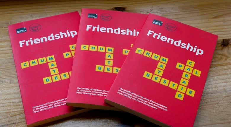 Three copies of the Book Week Scotland title, Friendship. The book cover is red, with white lettering for the title, Friendship, and yellow squares of letters laid out like a crossword, spelling associated friendship words- Chum, Mate, Bestie, Caraid, and Pal.