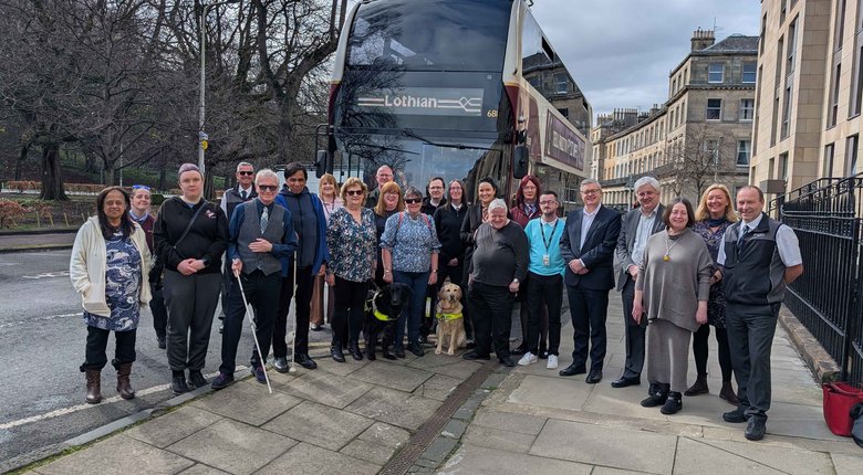A large group of bus drivers, volunteers, supporters and RNIB Scotland colleagues stand outside together, in front of a Lothian bus.
