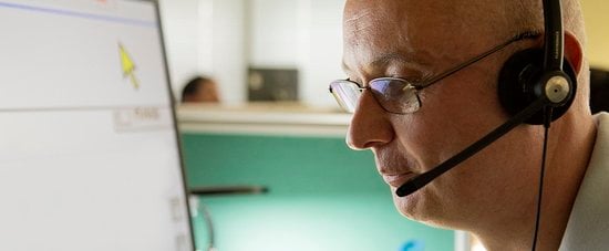 A Helpline and Sight Loss Adviser with a headset in front of computer screen.