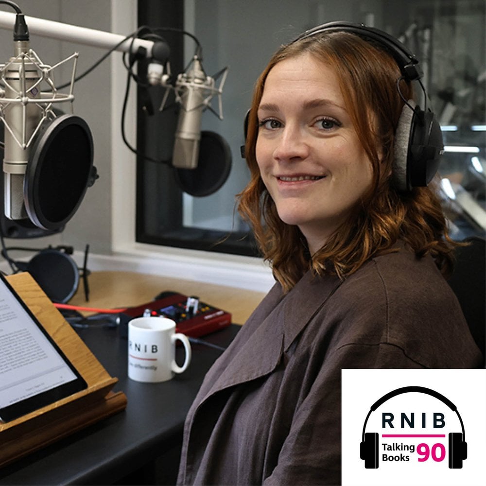 Charlotte Ritchie, a woman in her mid 30s sitting in a recording studio, turned to face the camera, smiling. she is wearing a dark brown blazer.