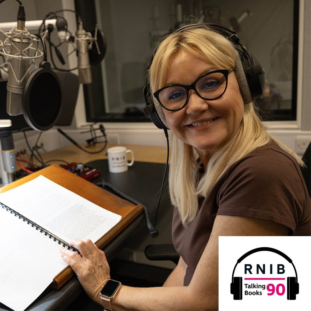 Lisa George, a woman in her mid 50s sitting in a recording studio, she is turned in her chair to face the camera smiling. She is wearing a brown t shirt and over ear headphones.