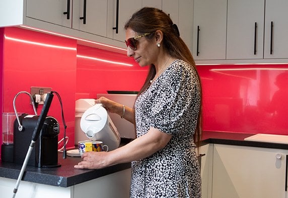 A woman with sight loss wearing a black dress with a white pattern, making a hot drink with a liquid level indicator, in an RNIB office kitchen.