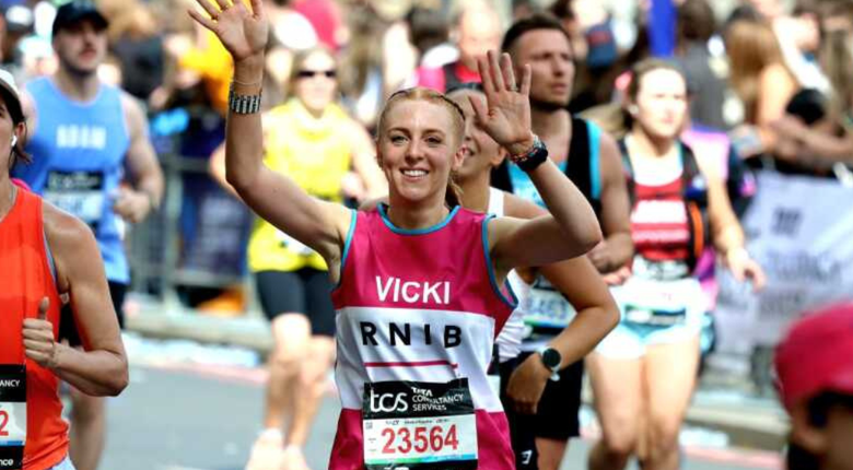 Vicki Paige crossing the finishing line at the London Marathon for RNIB.
Vicki is crossing the finishing line with both hands in the air. She is wearing a pink RNIB running vest and has light brown hair tied back in a bun. She is smiling. In the background are other runners and crowds of people cheering the runners on.