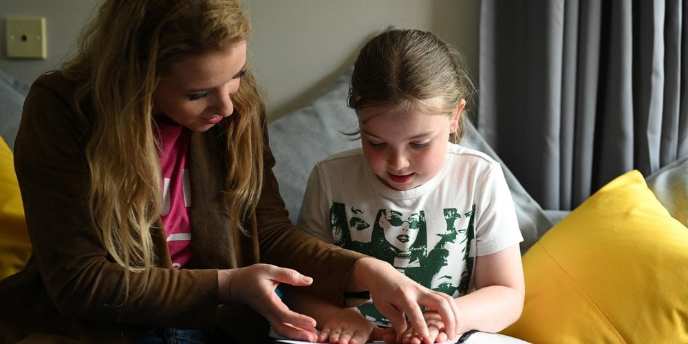 Image shows an adult guiding a child's hands across a book.