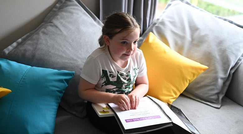 Image shows a child reading a braille and text certificate