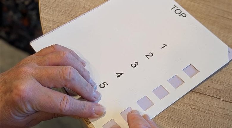 Hands reading the braille on a ballot paper card overlay while voting
