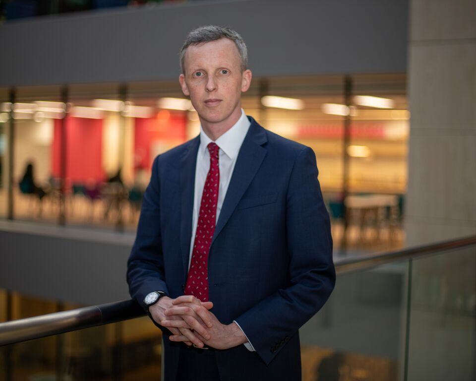 A picture of Andrew McCracken, a man with grey hair and a navy suit with red tie, looking at the camera