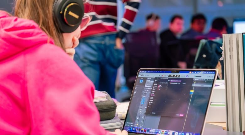 Person wearing a pink hoodie codes at a laptop during RNIB Game Jam