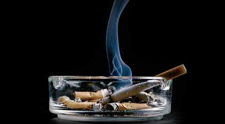 An ashtray of cigarettes with smoke against a black background.