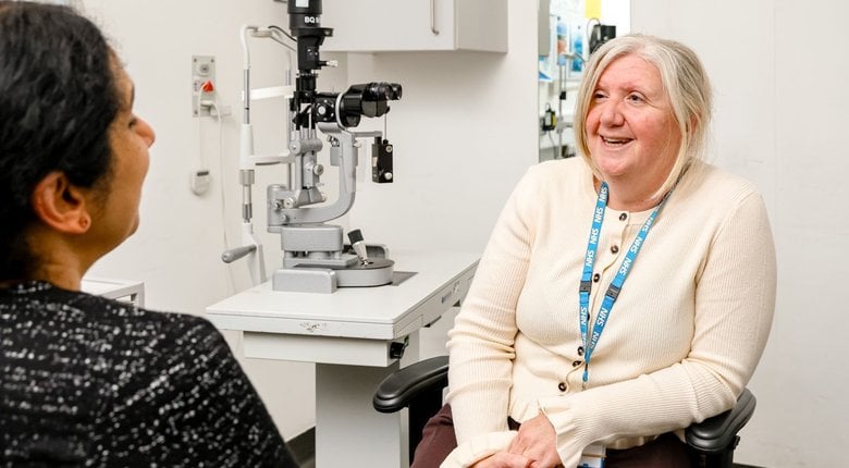 RNIB ECLO Lynda Daddario pictured at the Lister Hospital in Stevenage during the official launch of the ECLO service here. Linda is seated facing the camera. She has shoulder length grey hair and is smiling and to her right is a piece of optical equipment. She is wearing a cream-coloured cardigan.