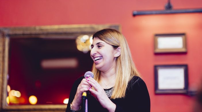 Tafsila Khan on stage holding a microphone and laughing.