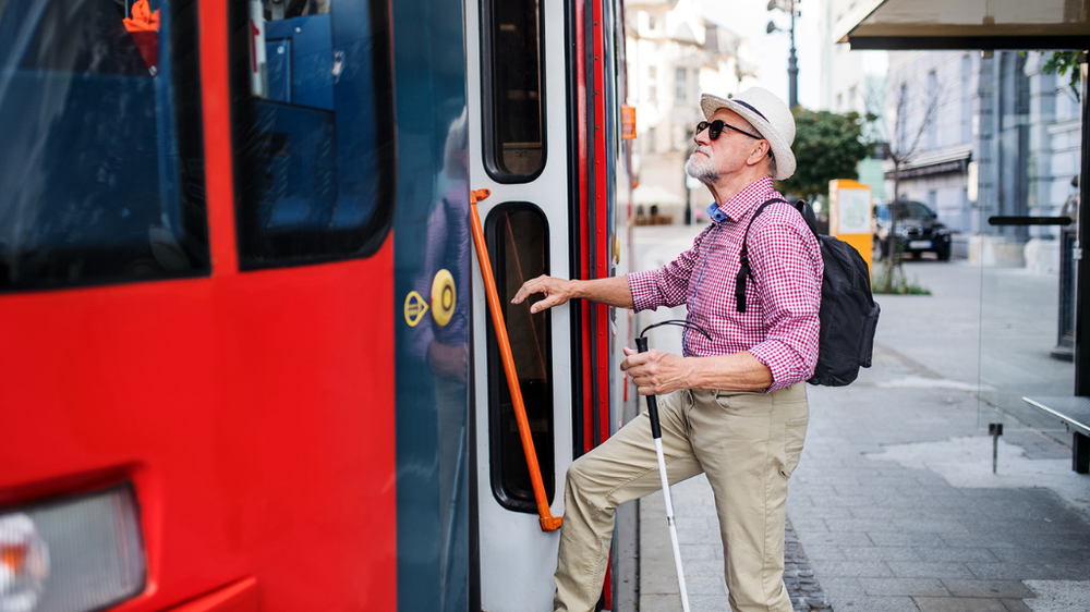 A senior blind man with a white cane getting on a public bus.