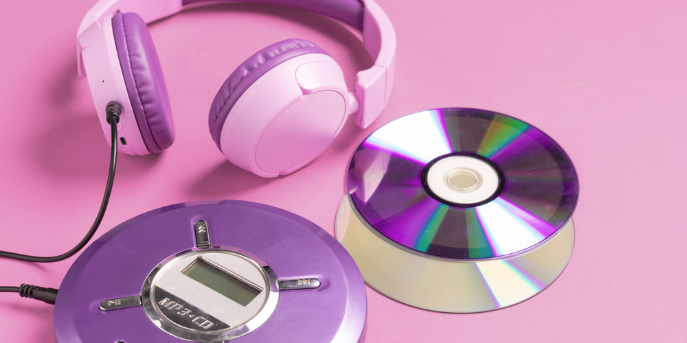 Against a dark pink background a purple CD player with light pink headphones and a couple of CDs.