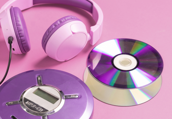 Against a dark pink background a purple CD player with light pink headphones and a couple of CDs.