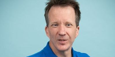 Close up of Toby standing in front of a light background wearing a blue top
