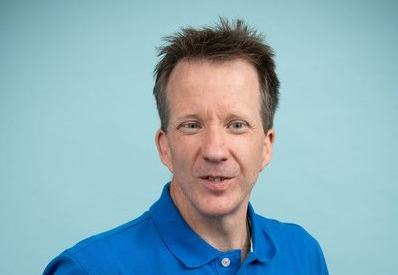 Close up of Toby standing in front of a light background wearing a blue top