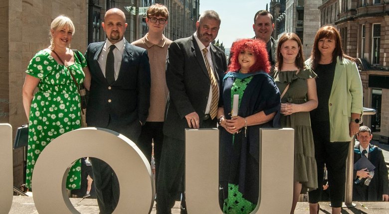 Eight people stood in a line. One of them is wearing graduation robes.