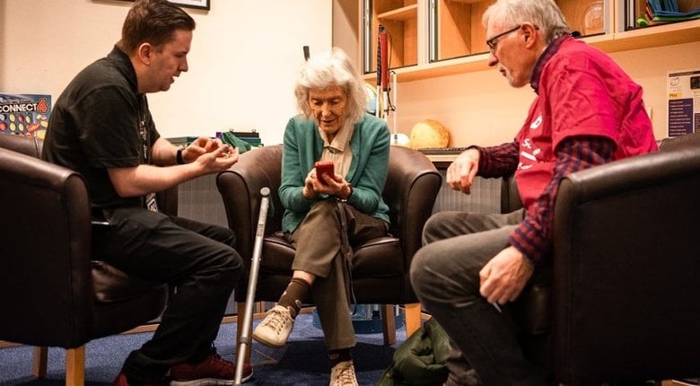 A member of RNIB staff and an RNIB volunteer help a customer to understand their smartphone.