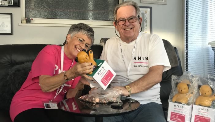 RNIB volunteers Alan and Janet on a sofa, smiling and counting donations from Sooty Boxes.