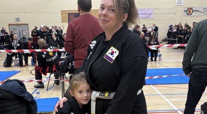 Amanda and her daughter stand together, both wearing martial art gis, smiling.