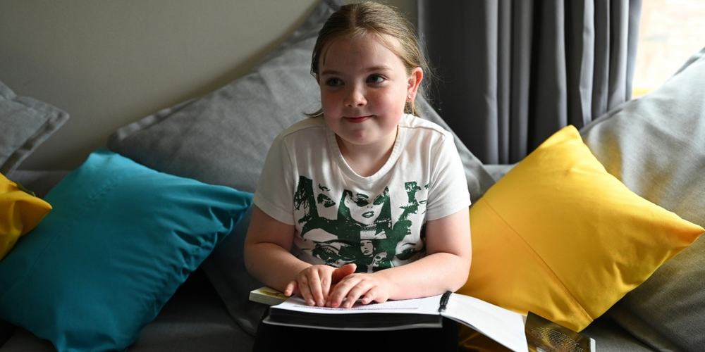 A young girl sitting on a sofa reading a book